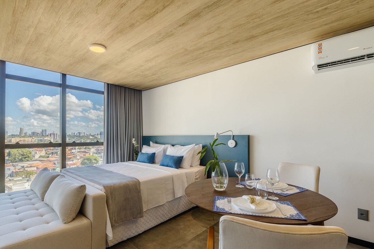 A modern hotel room with a large bed, a dining table set for two, and a city view.