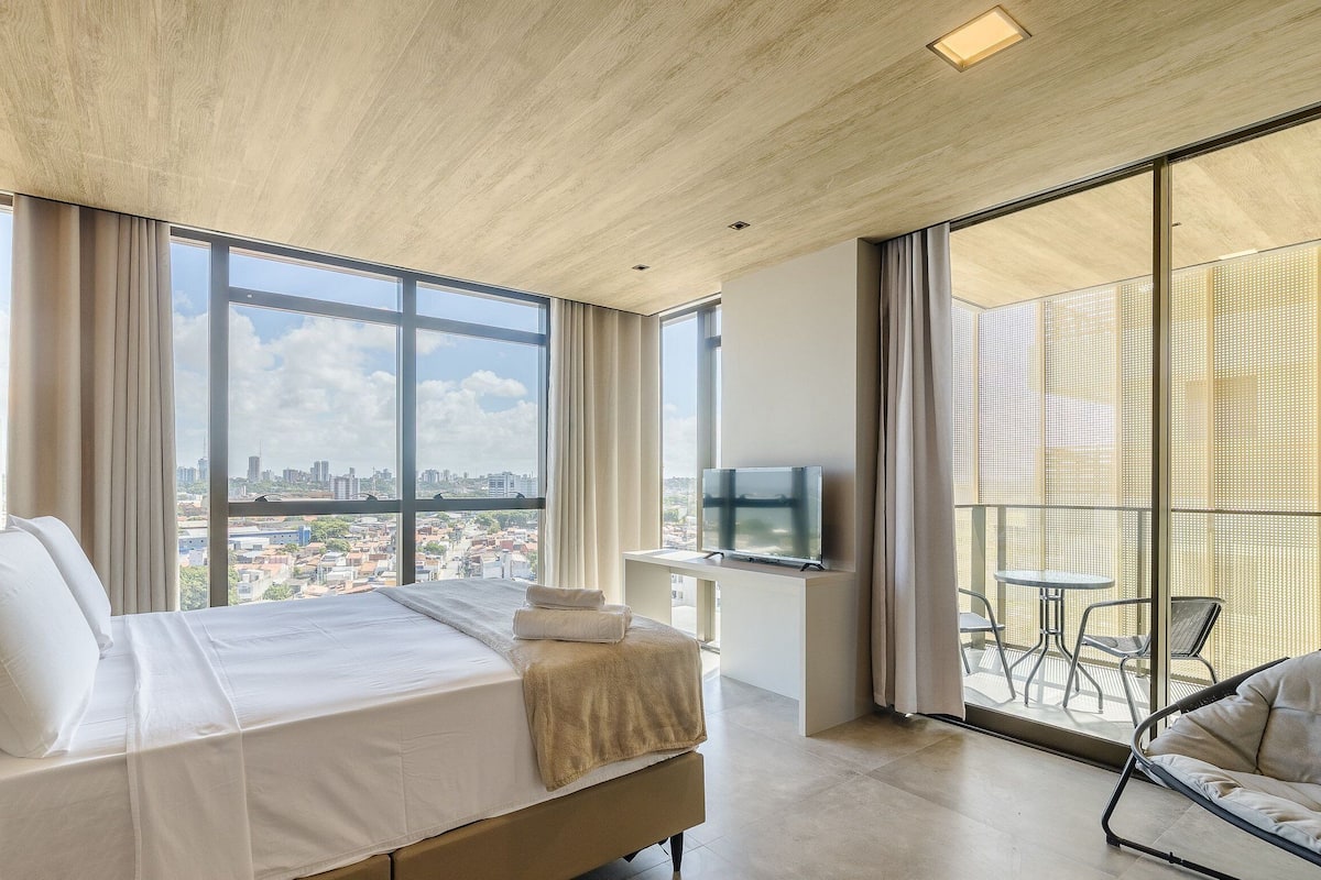 Una habitación de hotel moderna con una cama grande, televisión y un balcón con mobiliario exterior.