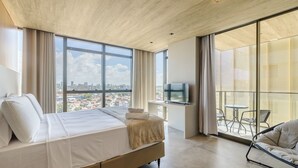 A modern hotel room with a large bed, a TV, and a balcony with outdoor seating. - Nwts - Studios With Side sea View in Maceio III (Maceió)