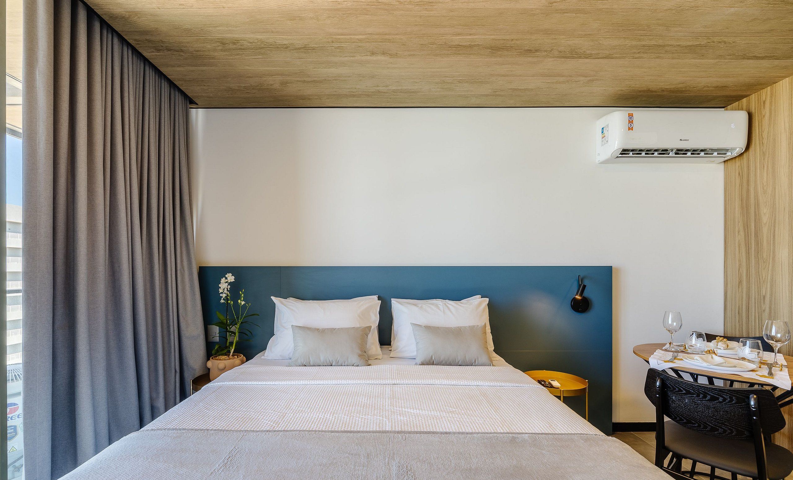 Une chambre d’hôtel équipée d’un lit, d’une table de chevet, d’une table dressée pour le repas et d’un appareil de climatisation.