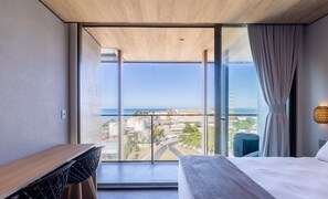 Een moderne hotelkamer met een ruim balkon, een bed, een bureau en uitzicht op de stad en zee.