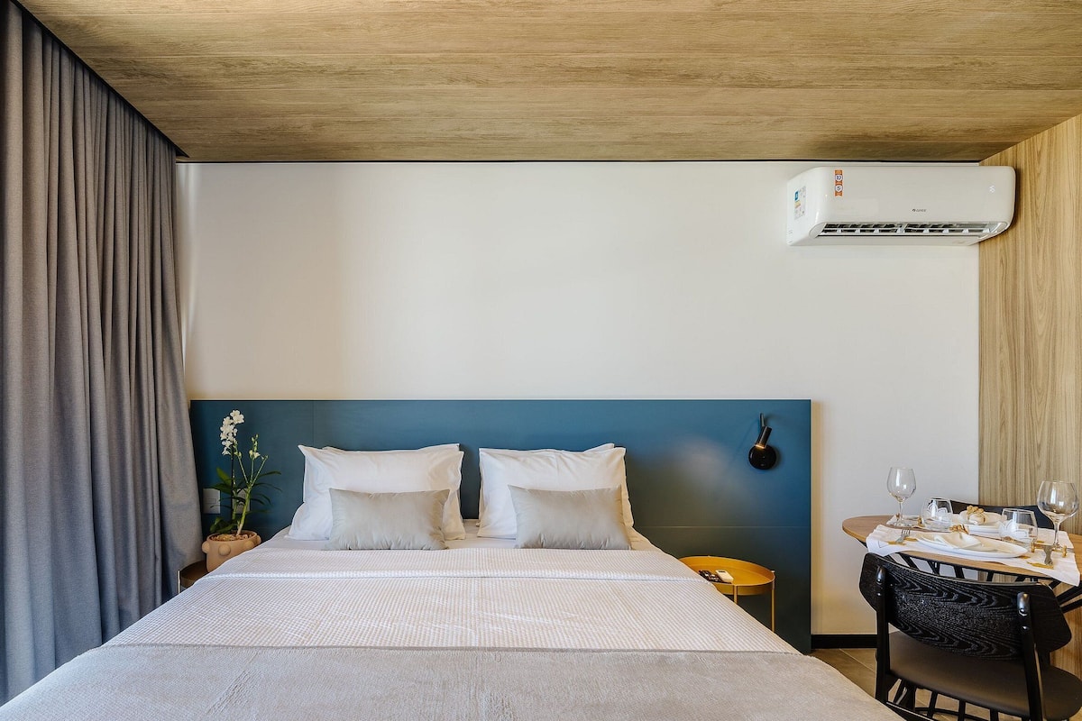 Una habitación de hotel con cama, mesita de noche, mesa lista para cenar y un equipo de aire acondicionado.