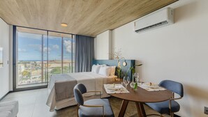 A hotel room with a bed, a dining table with chairs, a view of the city through large windows, and an air conditioning unit on the wall. - Nwts - Studios With Side sea View in Maceio III (Maceió)