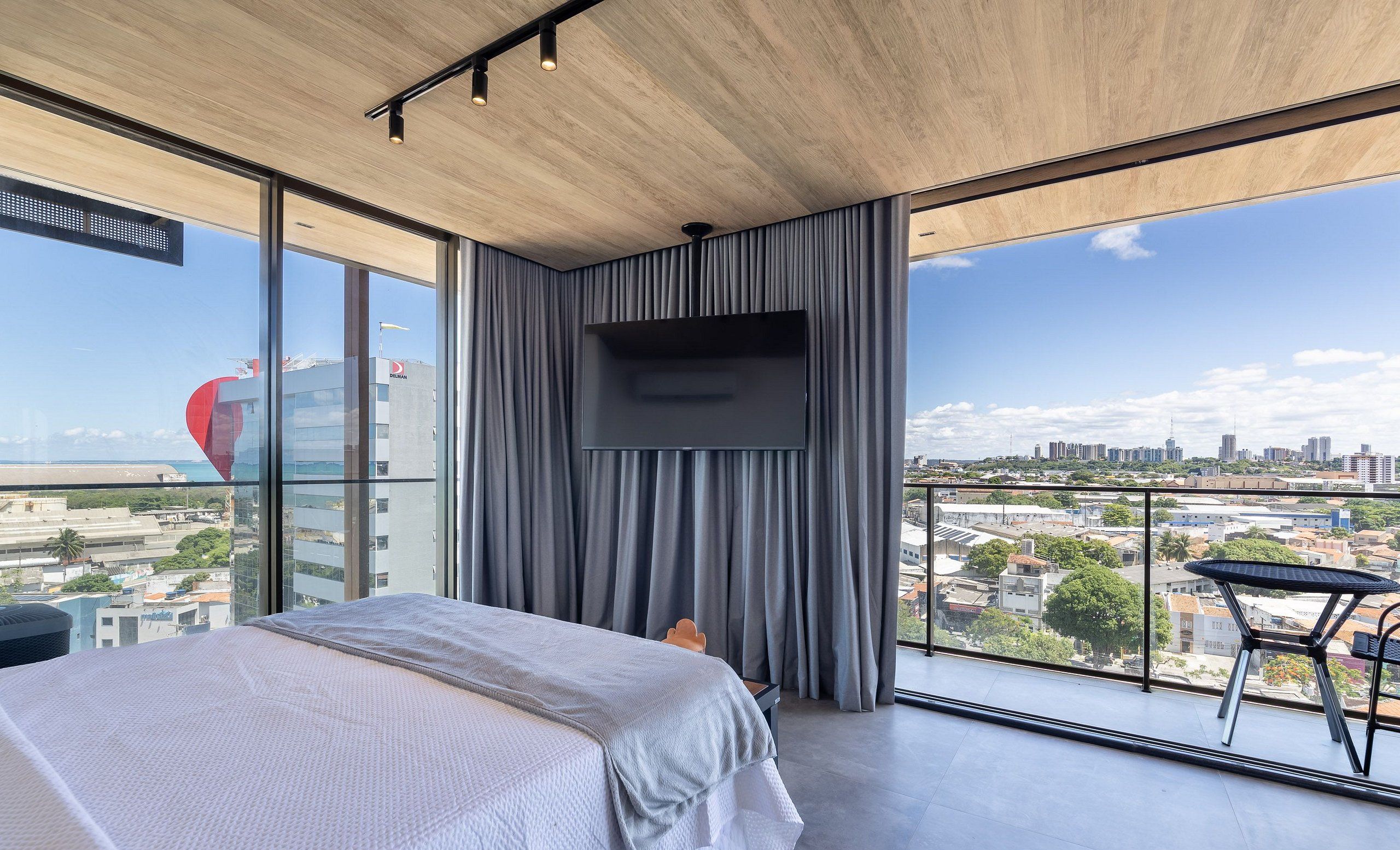 Un dormitorio moderno con una cama grande, un televisor montado en la pared y un balcón con vistas a la ciudad.