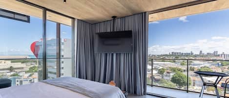 Un dormitorio moderno con una cama grande, un televisor montado en la pared y un balcón con vistas a la ciudad.