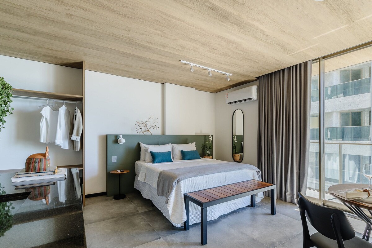 Una habitación de hotel moderna con cama, mesita de noche, banco y zona de comedor con mesa y sillas.