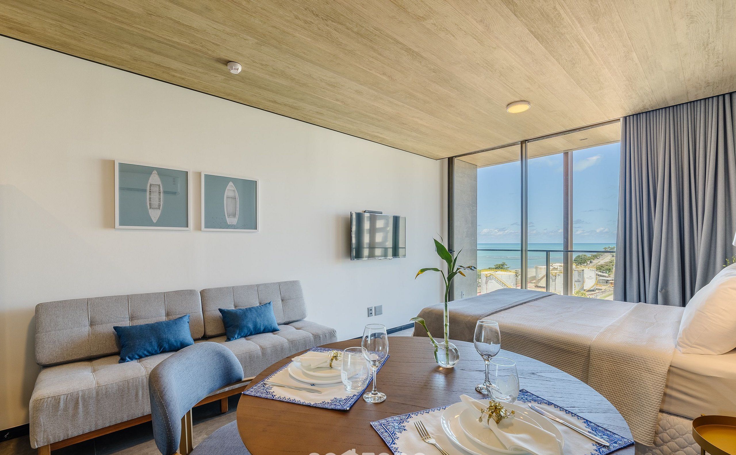 Ett modernt hotellrum med ett stort fönster som erbjuder utsikt över havet, en soffa, ett matbord för två personer och en säng.