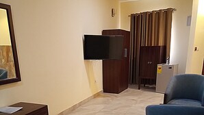 A hotel room with a bed, a desk, a chair, a television, and a wardrobe. - BowMarie Resort (Kpandai)
