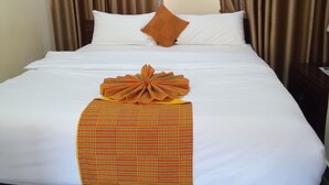 A neatly made bed with white linens, a brown headboard, and a decorative orange bow on the bed. - BowMarie Resort (Kpandai)