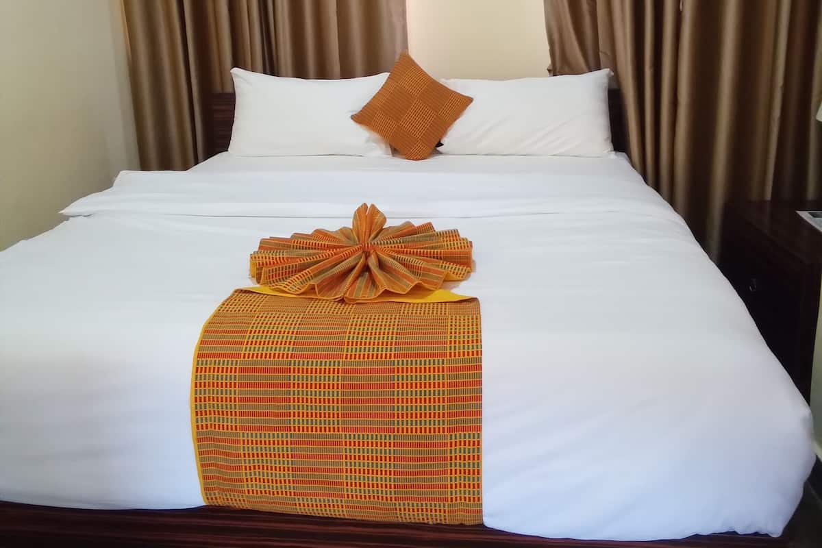 A neatly made bed with white linens, a brown headboard, and a decorative orange bow on the bed.