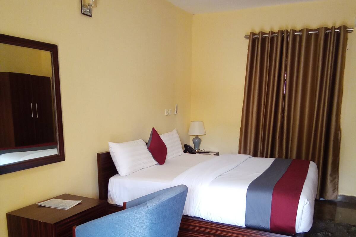 A hotel room with a bed, a desk, a chair, a ceiling fan, a lamp, and curtains.