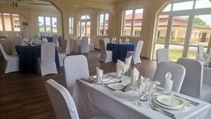 A banquet hall with tables set for dining, white chairs, and a view of the outside through large windows. - BowMarie Resort (Kpandai)
