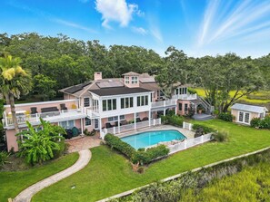 A large house with a swimming pool, multiple decks, and lush greenery. - Historic Marshfront St Simons Estate • Heated Pool • Private Dock (St Simons)
