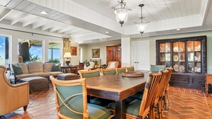 A spacious dining area with a large wooden table and wicker chairs, surrounded by a high ceiling with exposed beams and pendant lighting. - Historic Marshfront St Simons Estate • Heated Pool • Private Dock (St Simons)