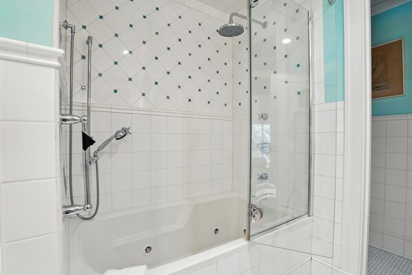 A glass-enclosed shower with a handheld showerhead and a handheld faucet.