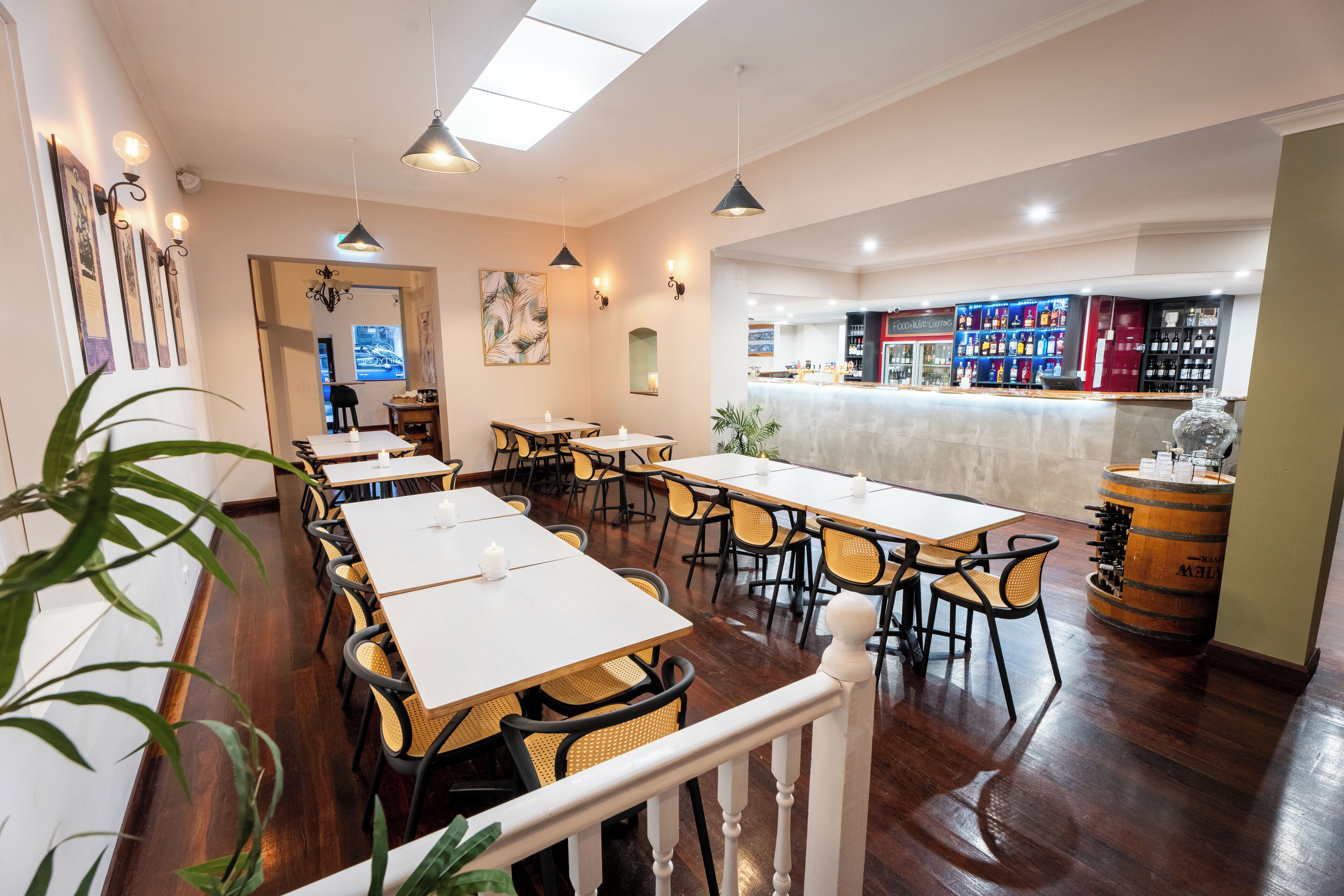 A restaurant with multiple tables and chairs, a bar area with shelves of bottles, and a wooden barrel.