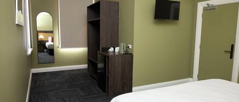 A hotel room with a bed, a desk, a mirror, a TV, and a door.