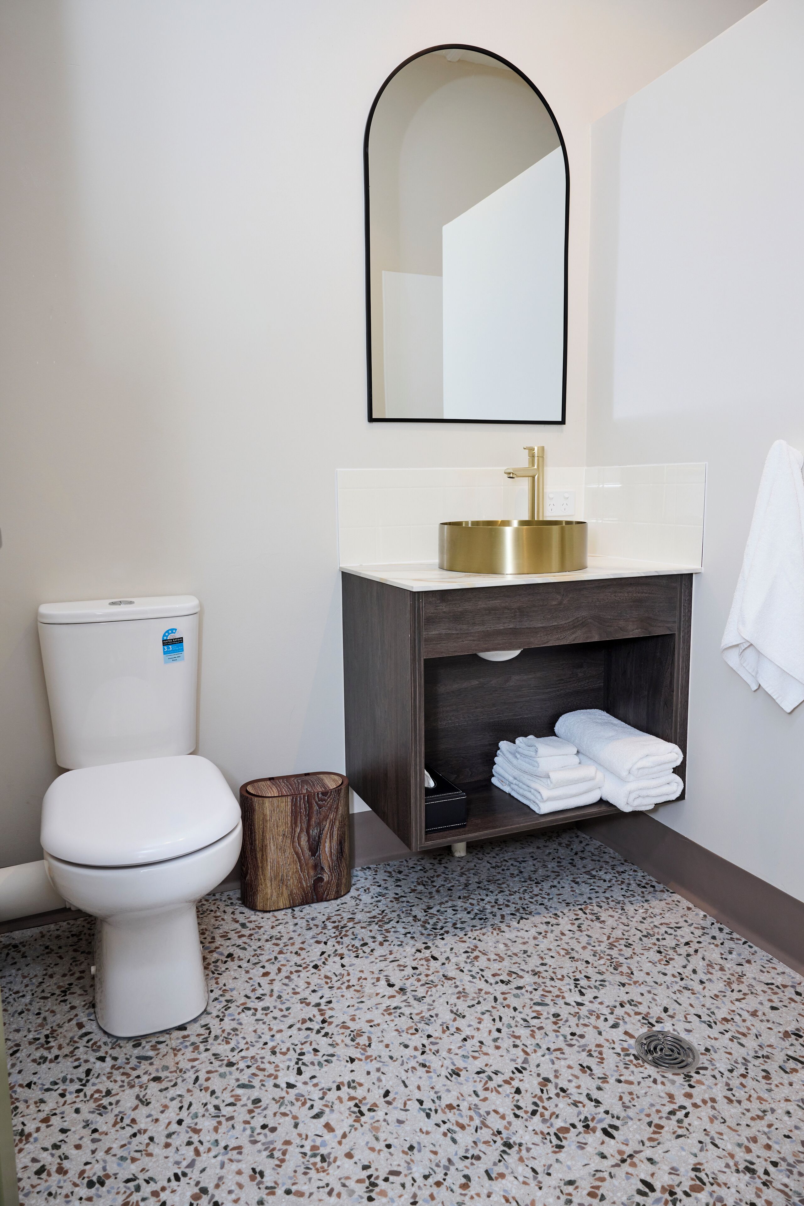 Un baño moderno con inodoro, lavabo de oro y tocador de madera, además de un espejo.