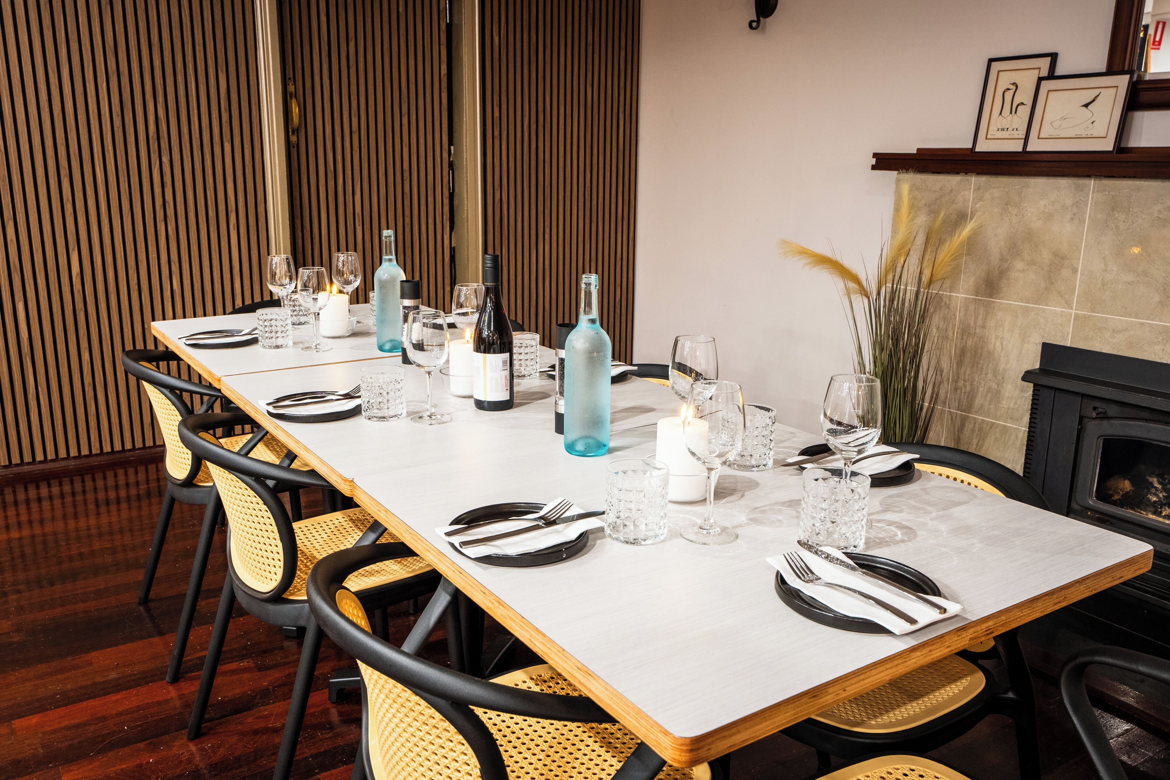 A dining table set with wine glasses, bottles, and candles, surrounded by wicker chairs.