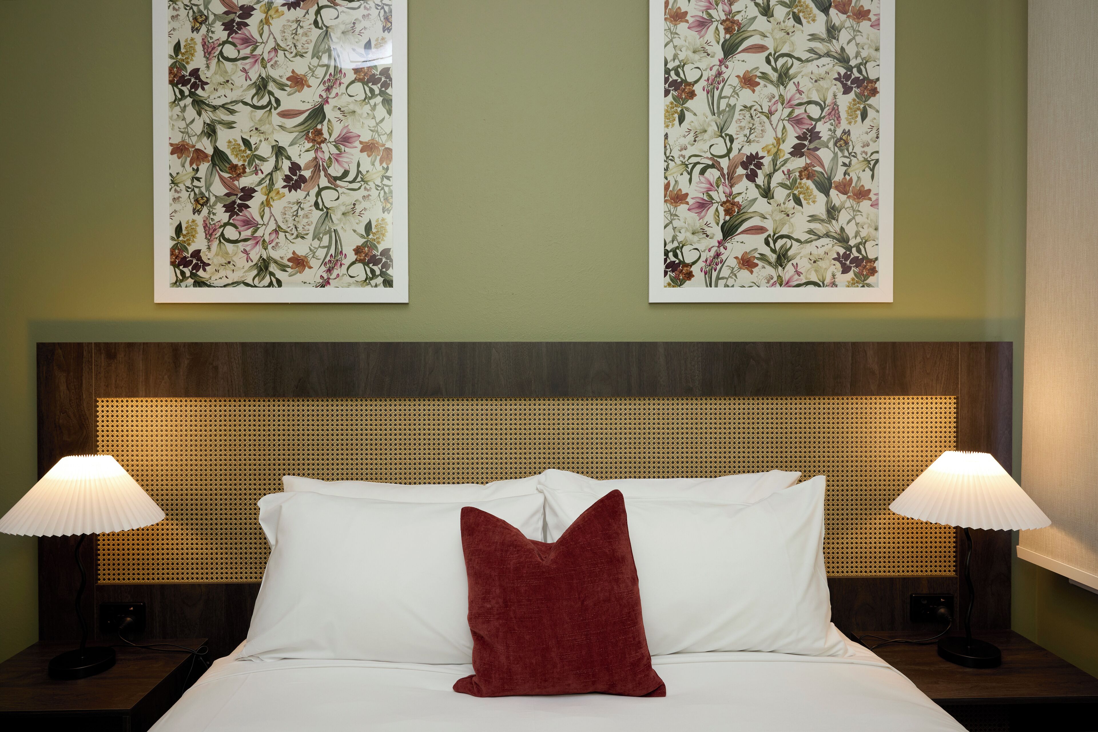 Una habitación de hotel con una cama, dos mesitas de noche, dos lámparas y dos cuadros con motivos florales.