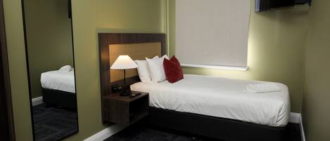 A hotel room with a single bed, a nightstand with a lamp, a TV mounted on the wall, and a large mirror.