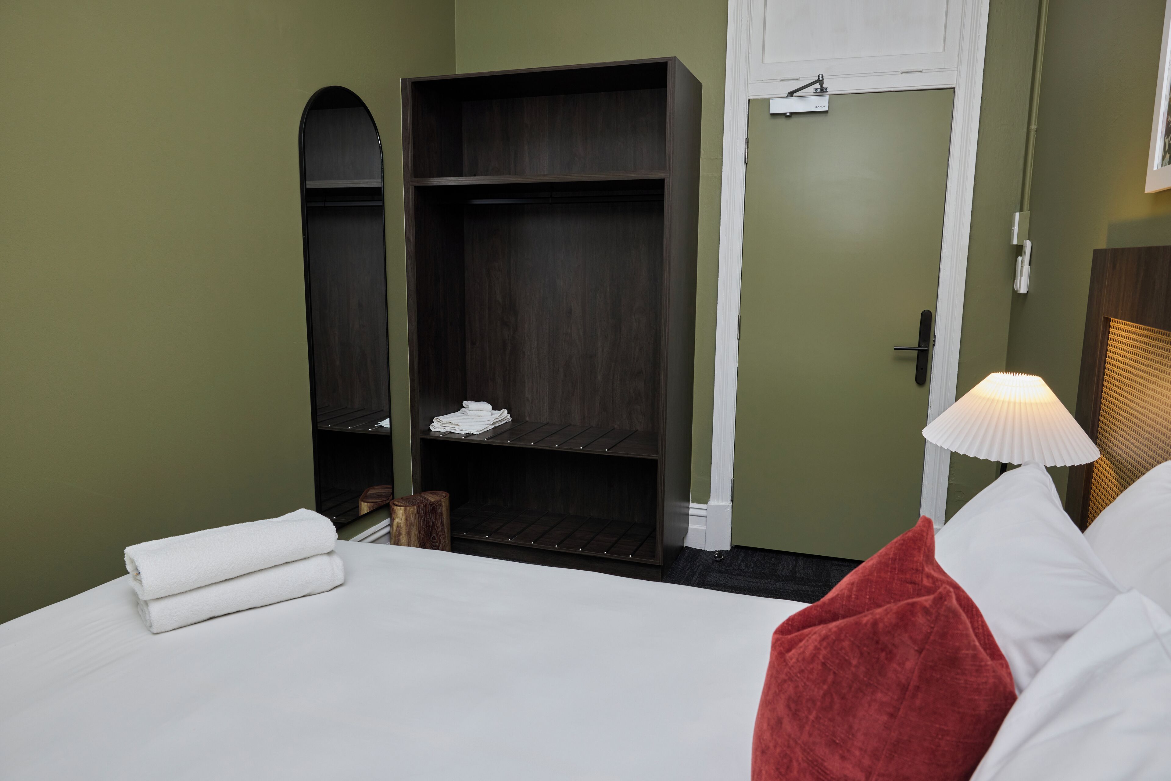 Una habitación de hotel con cama, armario y mesita de noche con lámpara.