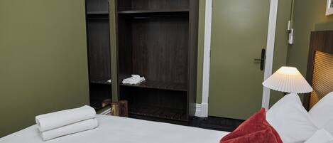 A hotel room with a bed, a wardrobe, and a nightstand with a lamp.