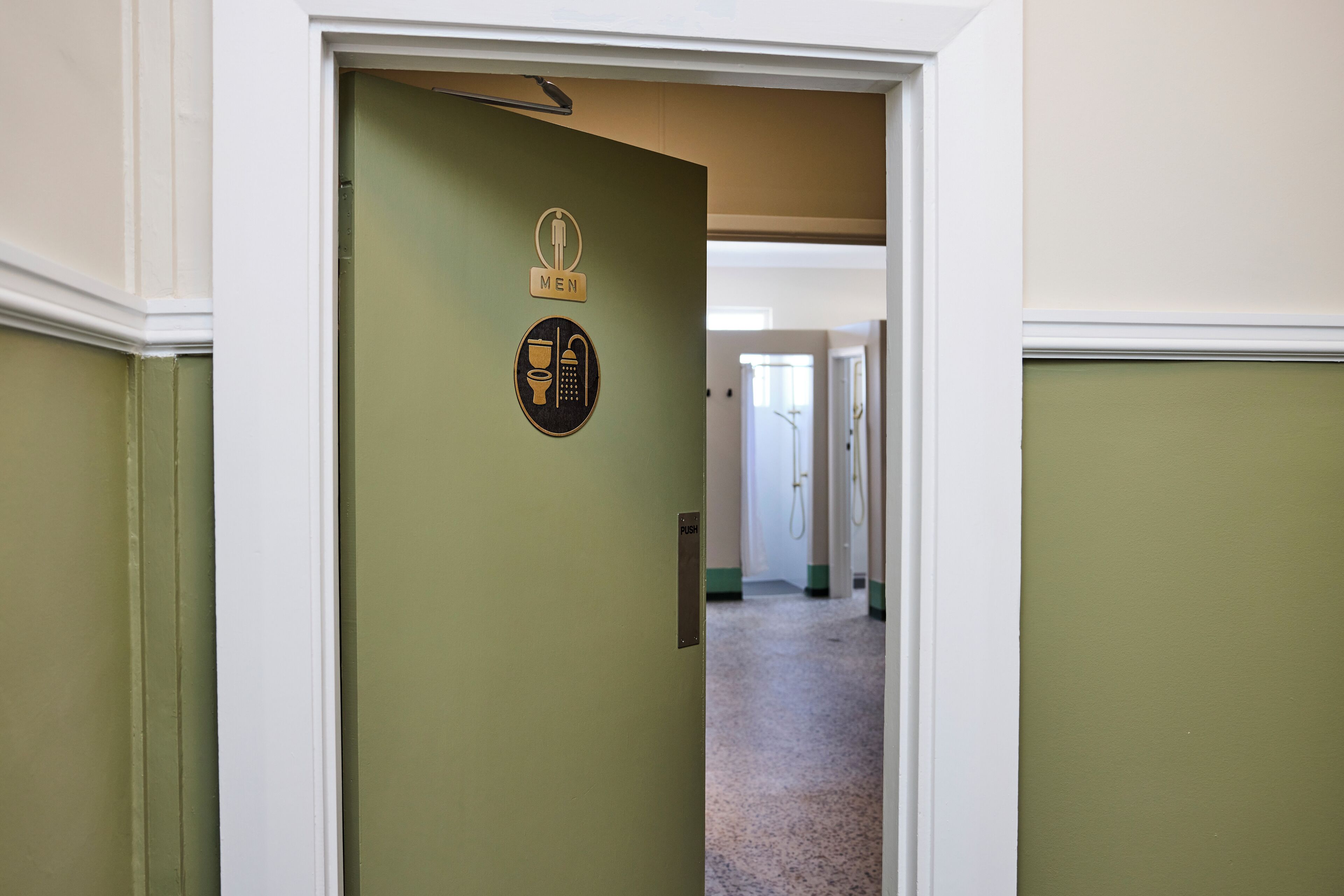 A hallway with a door marked "MEN" and a "PUSH" sign, leading to a room with a window and a door in the background.