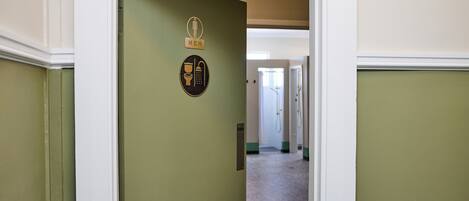 A hallway with a door marked "MEN" and a "PUSH" sign, leading to a room with a window and a door in the background.
