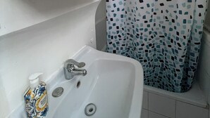 A bathroom with a white sink, a hand soap dispenser, and a shower curtain with a mosaic pattern.