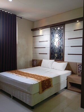 A neatly arranged bedroom with a large bed, a decorative headboard, and a small bedside table. - Graha Laweyan Solo (Surakarta)
