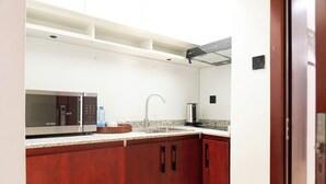 A compact kitchen with a microwave, sink, and stainless steel kettle. - The Meridian Apartments Abuja (Abuja)