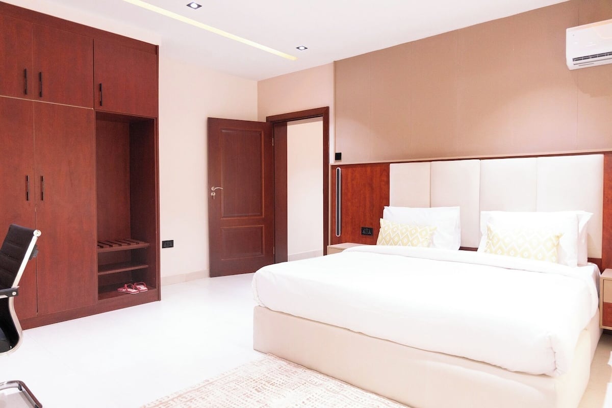 A bedroom with a large bed, a wardrobe, a chair, and a door.