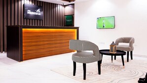 A reception area with a wooden reception desk, two patterned chairs, a small table, and a TV mounted on the wall. - The Meridian Apartments Abuja (Abuja)