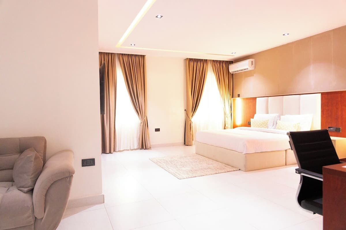 A modern hotel room with a bed, a desk, a chair, and a sofa.