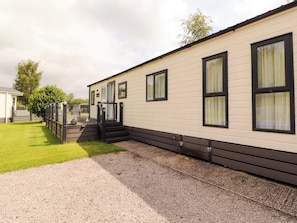A mobile home with a front porch, a gravel driveway, and a grassy yard.