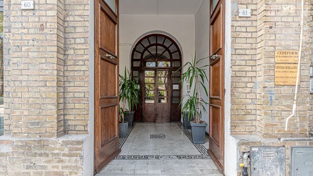 Une entrée d’immeuble avec une porte en bois, des plantes en pot et un sol carrelé.