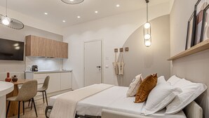 Une chambre d’hôtel moderne équipée d’un lit, d’un petit bureau, d’une chaise, d’une télévision et d’une kitchenette.