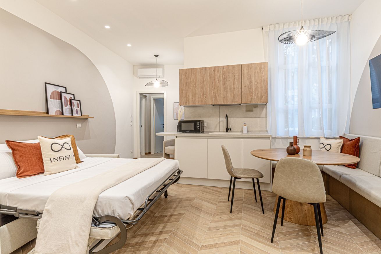 Espaço compacto para relaxar, com cama, cozinha compacta, área de refeições e janela com cortinas.