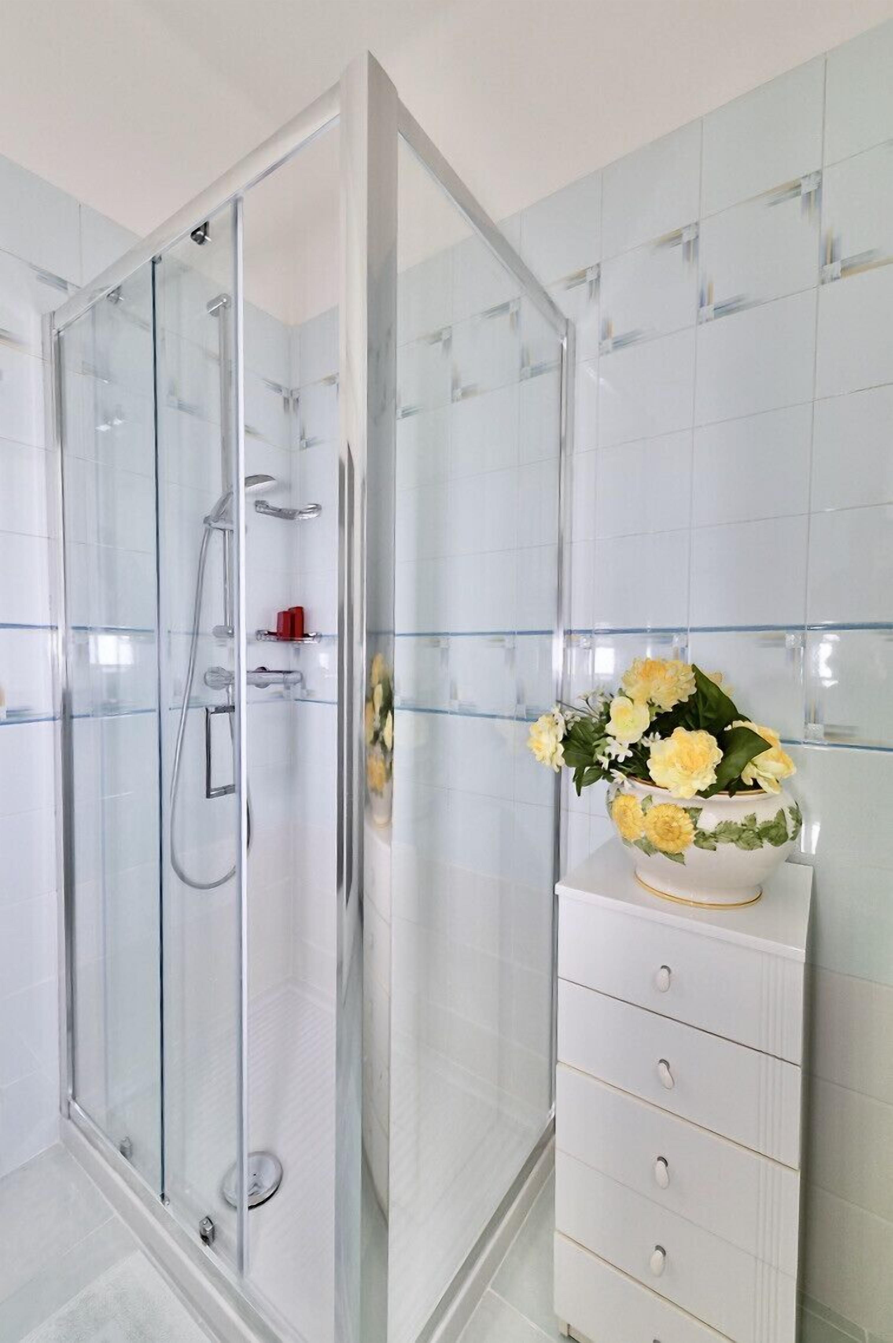 Een moderne badkamer met een douchecabine van glas, witte betegelde wanden en een wit kastje met lades.