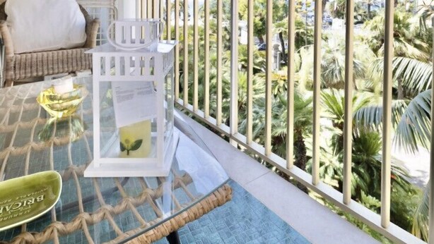 Un balcone con tavolo in vetro, sedie in vimini e un tendone a righe.