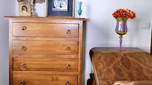 Un comò di legno con diversi cassetti, un quadro incorniciato, una lampada e un vaso con fiori su un tavolo.