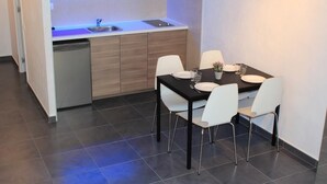 A compact kitchen with a built-in dishwasher, a small dining table with four white chairs, and a single light fixture above the countertop. - Villa Sagrada (Barcelona)