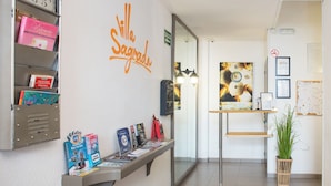 A reception area with a clock, a sign reading "Villa Sagredo," and a display of travel brochures. - Villa Sagrada (Barcelona)