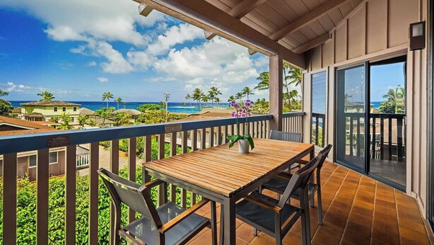 Un balcón con mesa y sillas de madera, con vista a una playa con palmeras y casas.