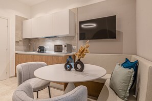A modern kitchen with white cabinets, a built-in oven, and a microwave. There's a round table with two chairs, a vase with dried flowers, and a flat-screen TV mounted on the wall. - Infinity Stay • Elegant Urban Escape (Civitanova Marche)