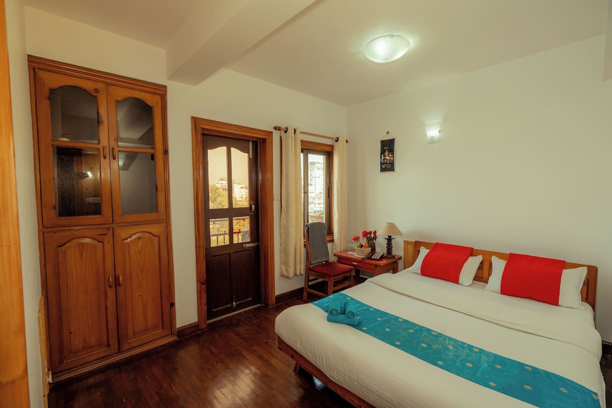 A bedroom with a large bed, wooden wardrobe, and a desk with a chair.