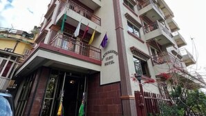 Un hôtel à plusieurs étages doté d’une entrée principale, de balcons et d’un mât où flotte un drapeau.