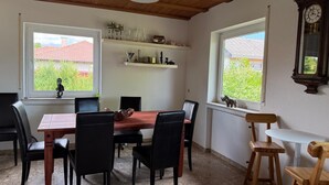 Un comedor con mesa y sillas de madera, una estantería con objetos decorativos y una ventana con vista a un edificio de tejados rojos.