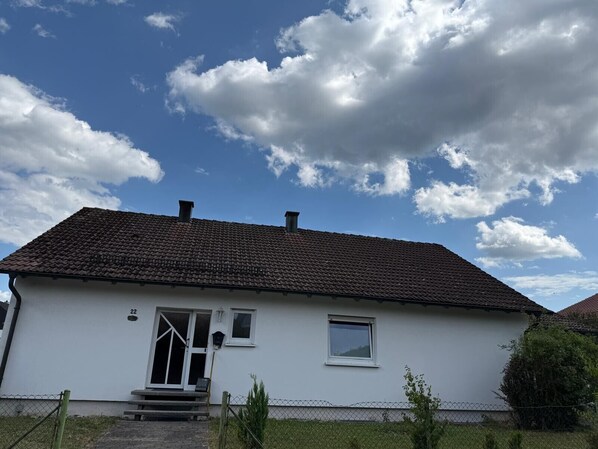 A single-story house with a tiled roof, a front door, a small window, and a number '22' on the wall.